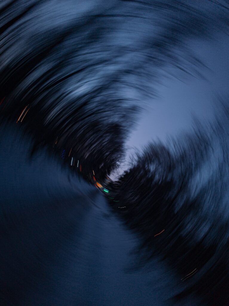 Current image: Swirling dark trees with distant lights at dusk